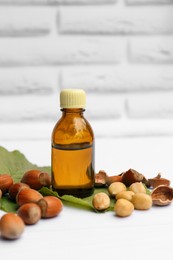 Photo of Bottle of hazelnut essential oil and nuts on white wooden table