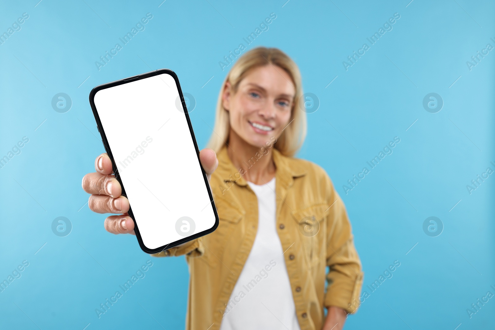 Photo of Happy woman holding smartphone with blank screen on light blue background, selective focus