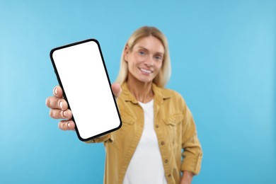 Happy woman holding smartphone with blank screen on light blue background, selective focus