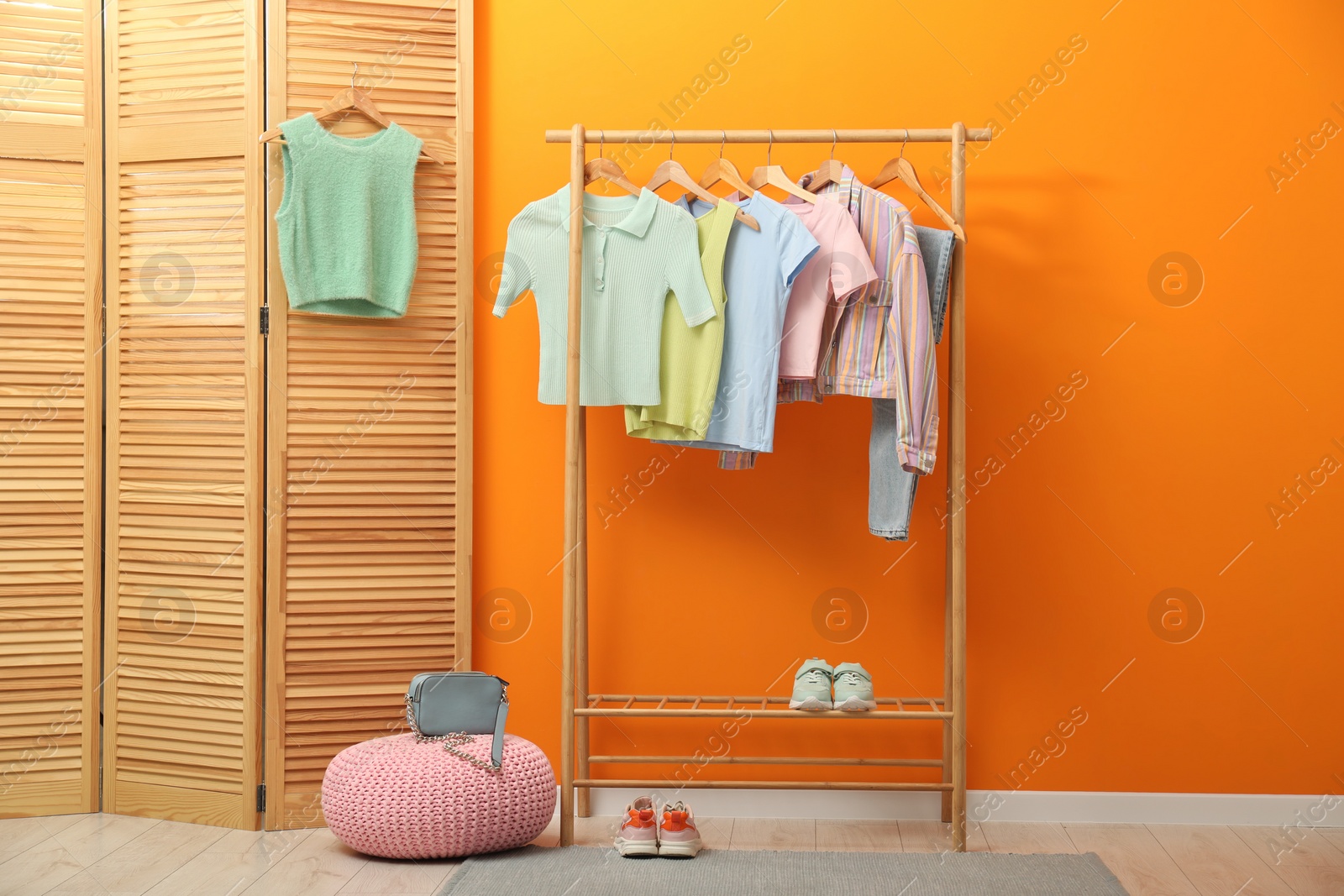 Photo of Rack with different stylish women's clothes, shoes, bag and pouf near orange wall indoors