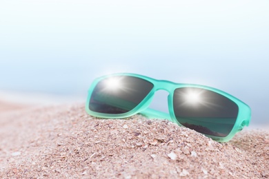 Stylish sunglasses on sandy beach near sea