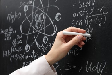 Photo of Teacher writing math formulas with chalk on blackboard, closeup