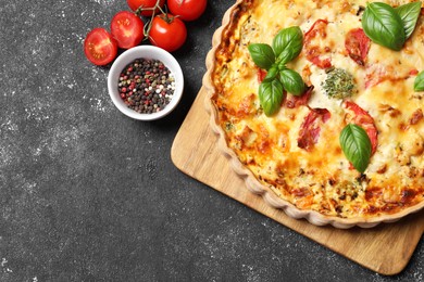 Photo of Tasty quiche with tomatoes, basil and cheese served on dark textured table, flat lay. Space for text