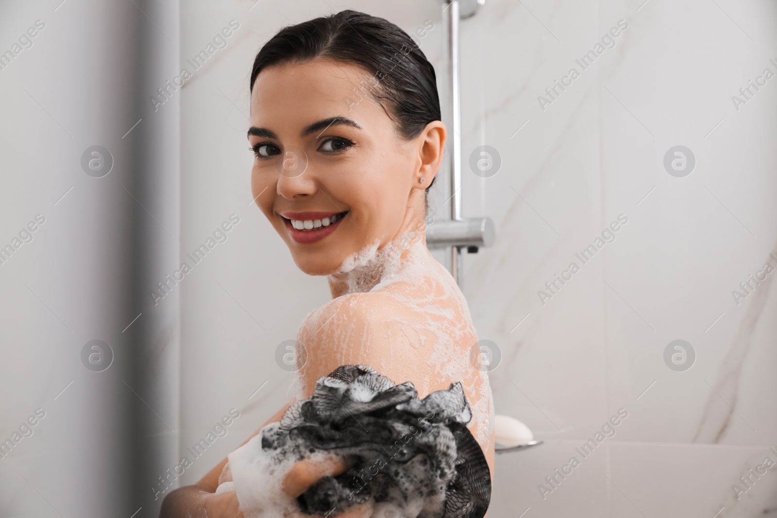 Photo of Young woman with mesh pouf taking shower at home