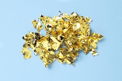 Photo of Many pieces of edible gold leaf on light blue background, top view