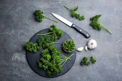 Fresh curly parsley, garlic and knife on grey table, flat lay