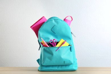 Bright backpack with different school stationery on wooden table against white background