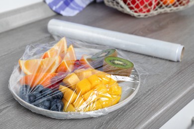 Plate of fresh fruits and berries with plastic food wrap on wooden table