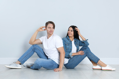 Photo of Young couple in stylish jeans sitting near light wall