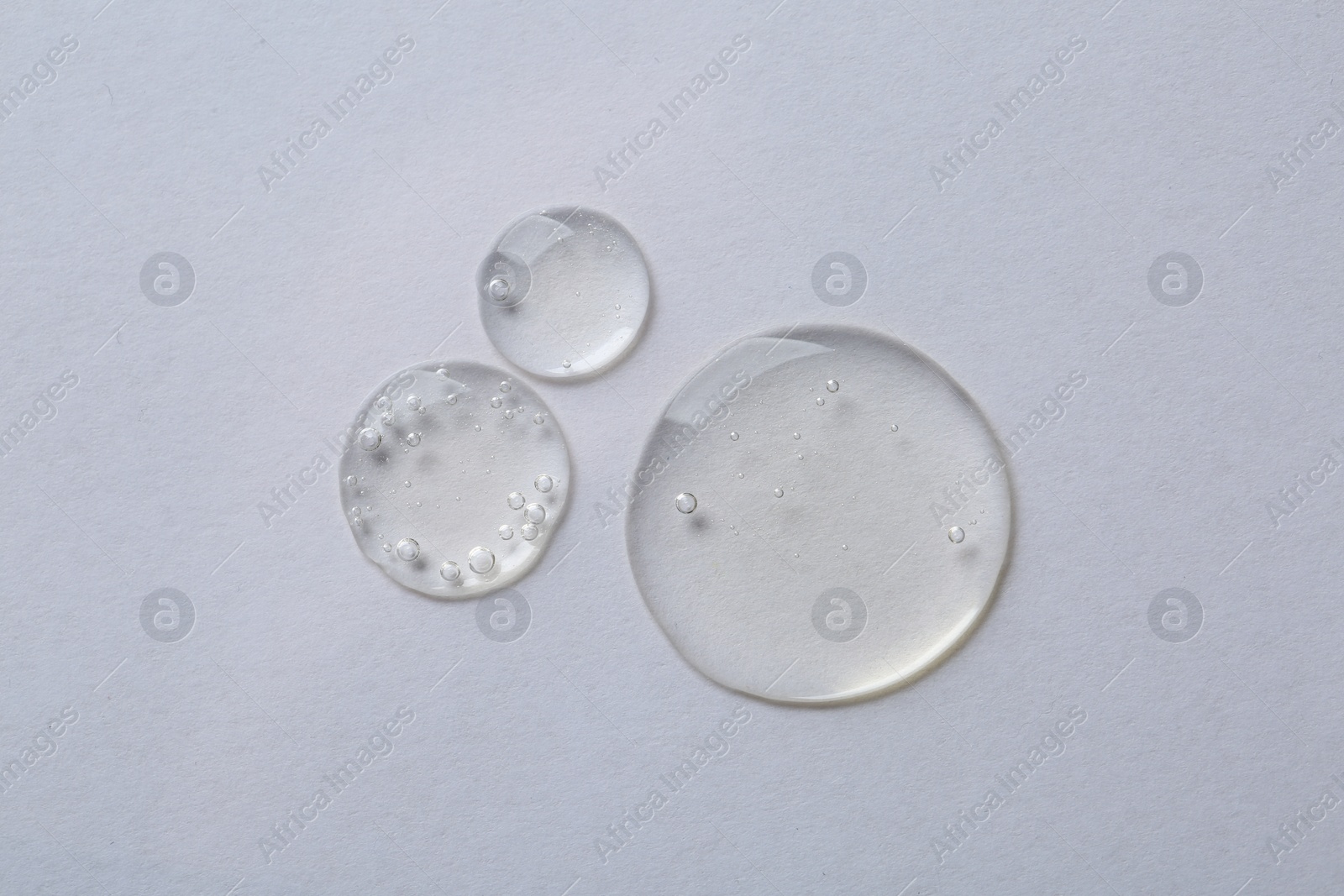 Photo of Drops of cosmetic serum on white background, top view