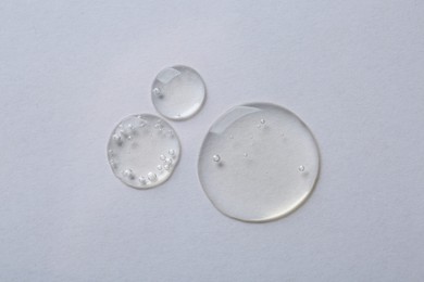 Photo of Drops of cosmetic serum on white background, top view