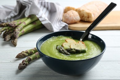 Photo of Delicious asparagus soup served on white wooden table