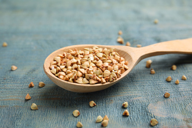 Uncooked green buckwheat grains in spoon on light blue wooden table, closeup