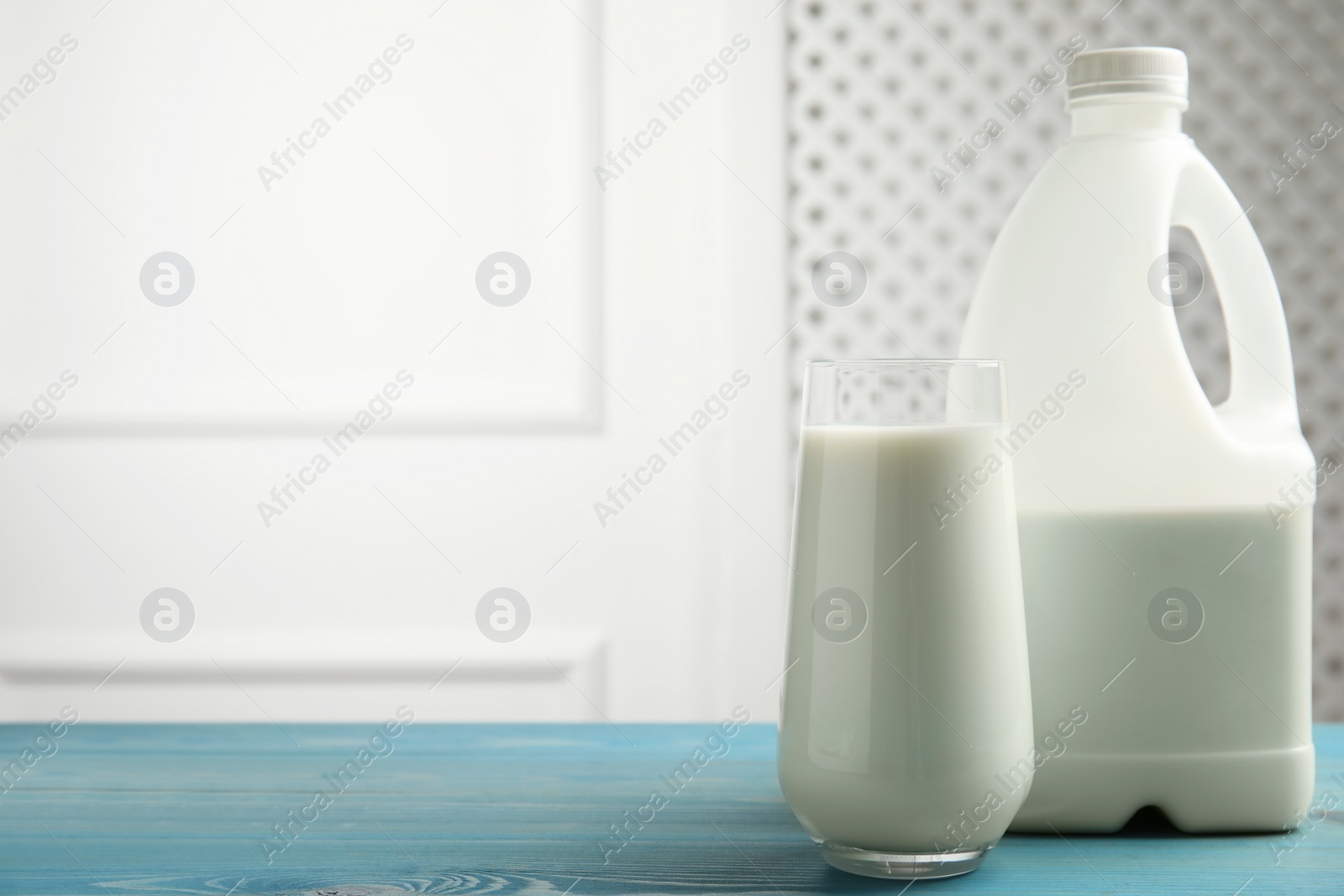 Photo of Gallon bottle and glass of milk on blue wooden table. Space for text