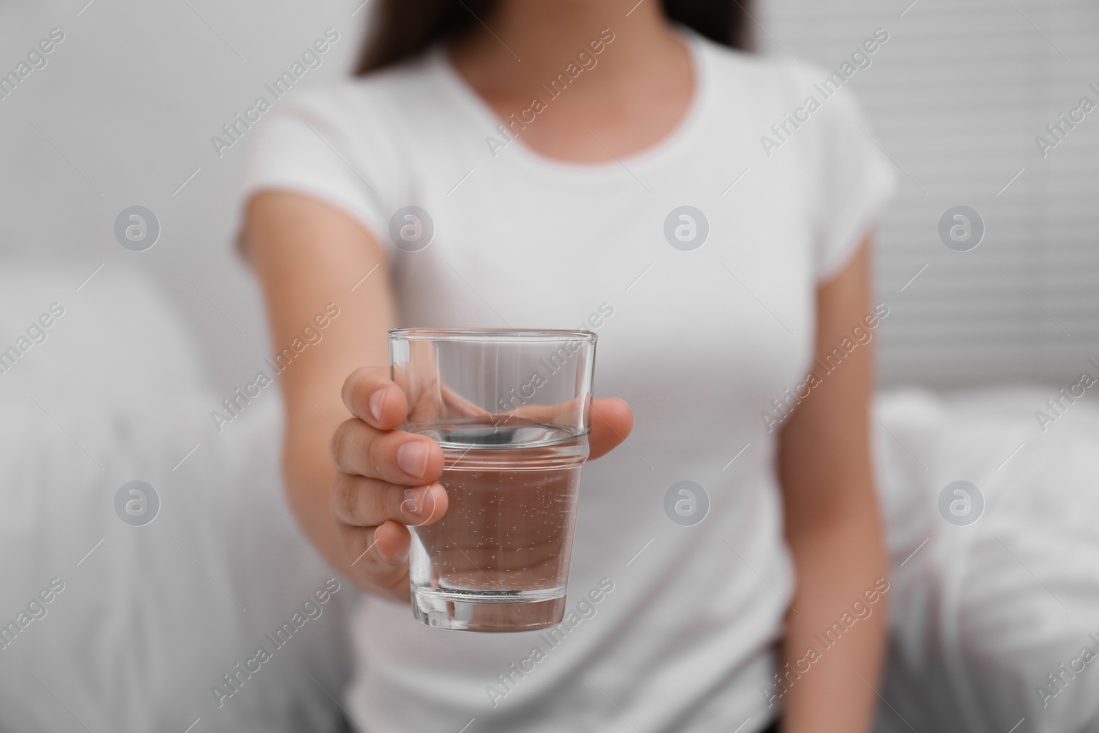 Photo of Woman holding glass of water in bedroom, closeup