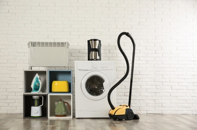 Photo of Modern vacuum cleaner and different household appliances near white brick wall indoors