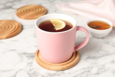 Mug of tea and stylish wooden cup coasters on white marble table