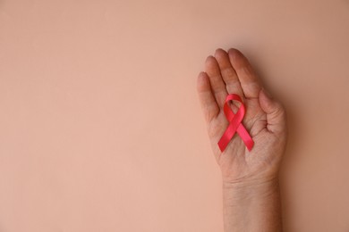 Senior woman holding pink ribbon on beige background, top view with space for text. Breast cancer awareness