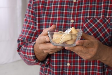 Photo of Man holding tasty fortune cookies with predictions indoors, closeup