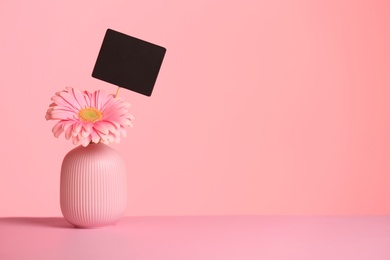 Photo of Vase with flower and empty card on table against color background, space for text. International Women's Day