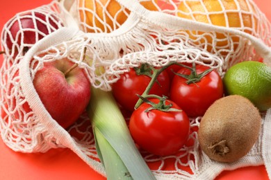 Photo of String bag with different vegetables and fruits on red background, closeup