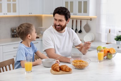 Photo of Father and his cute little son having breakfast at table in kitchen