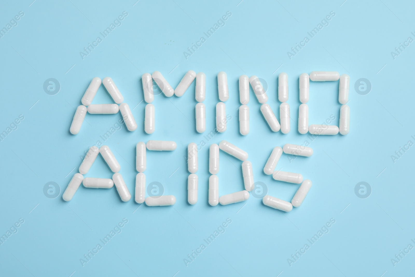 Photo of Phrase Amino acids made of pills on light blue background, flat lay