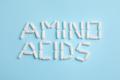 Phrase Amino acids made of pills on light blue background, flat lay