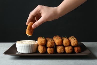 Photo of Woman dipping cheese stick into sauce at table, closeup