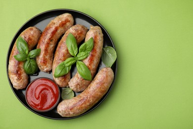 Plate with tasty homemade sausages, ketchup and basil leaves on green table, top view. Space for text