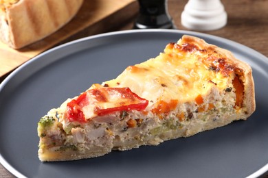 Piece of tasty quiche with chicken, cheese and vegetables on wooden table, closeup
