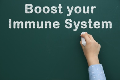 Image of Boost Your Immune System. Child writing text on green chalkboard, closeup