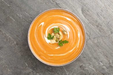 Delicious pumpkin soup with seeds and parsley in bowl on gray table, top view