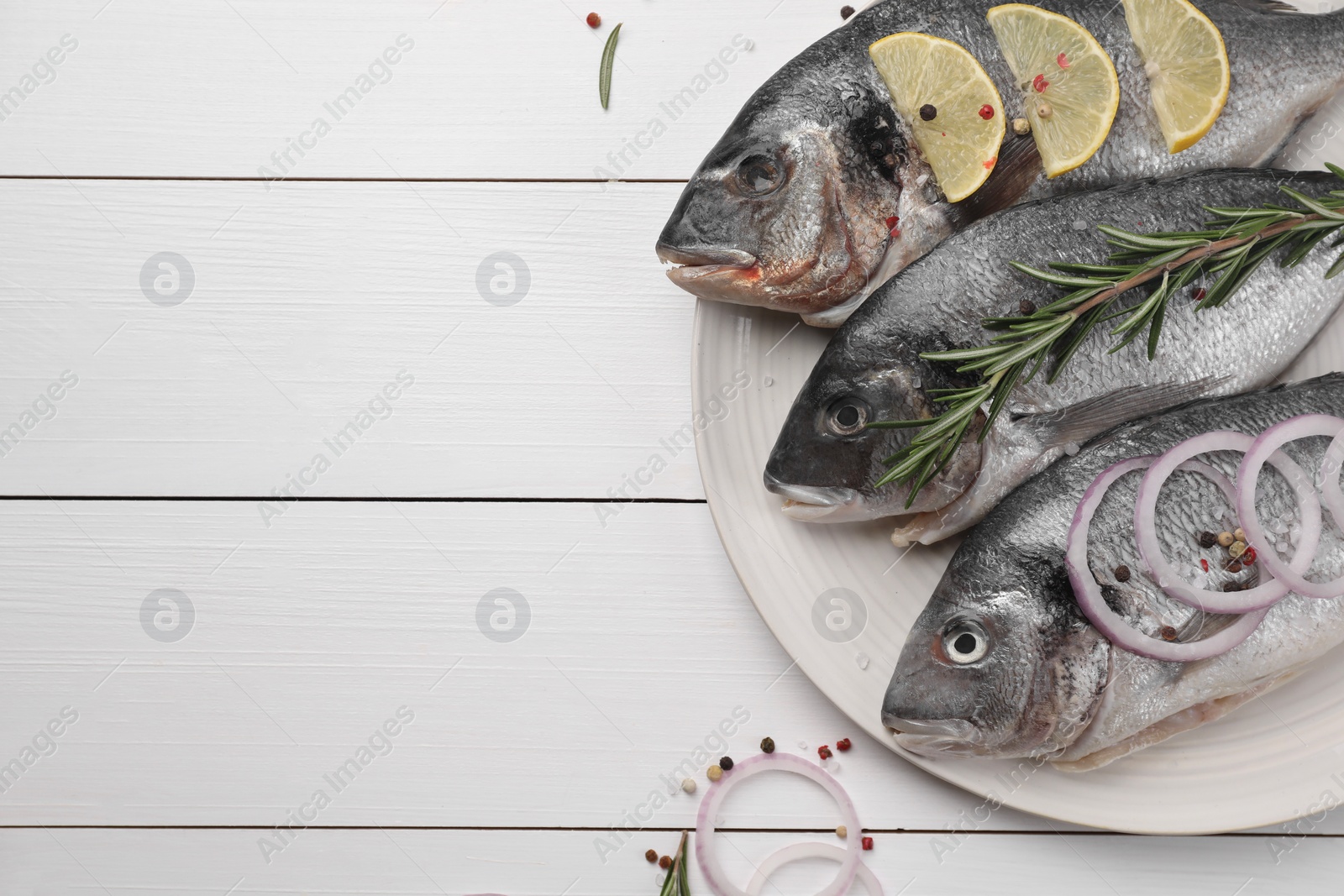 Photo of Raw dorado fish with lemon, rosemary and onion on white wooden table, flat lay. Space for text