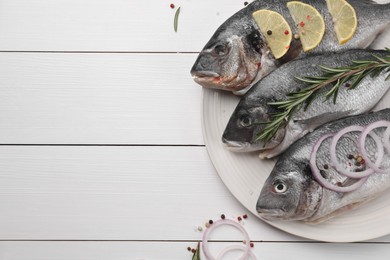 Photo of Raw dorado fish with lemon, rosemary and onion on white wooden table, flat lay. Space for text