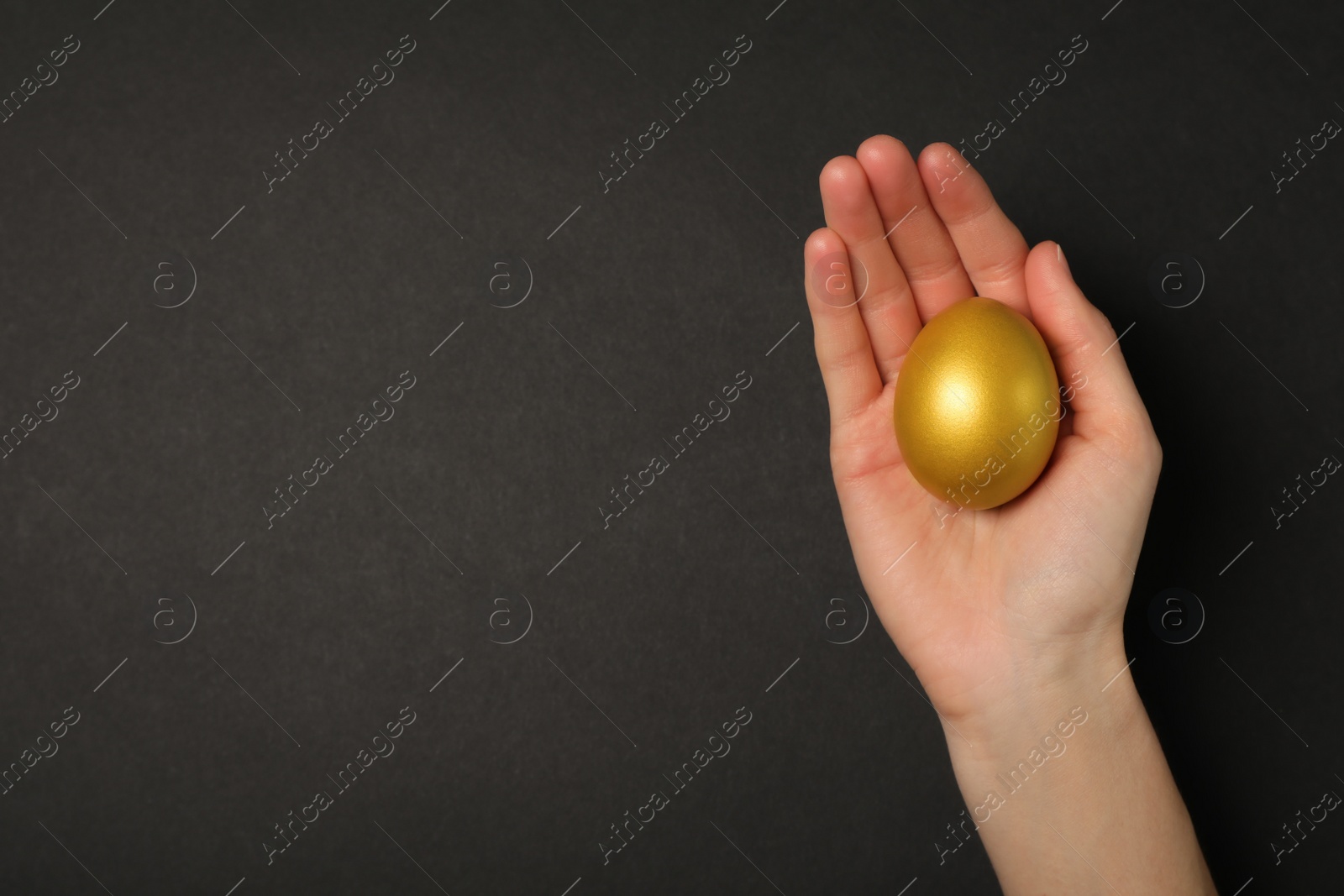 Photo of Woman holding shiny golden egg on black background, top view. Space for text