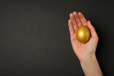 Photo of Woman holding shiny golden egg on black background, top view. Space for text