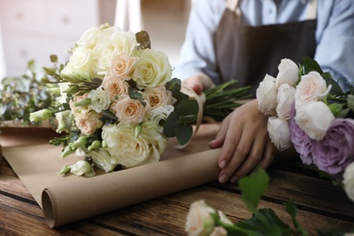 Photo of Florist wrapping beautiful wedding bouquet with paper at wooden table, closeup