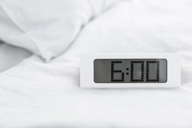 Photo of Digital alarm clock on bed. Time to wake up