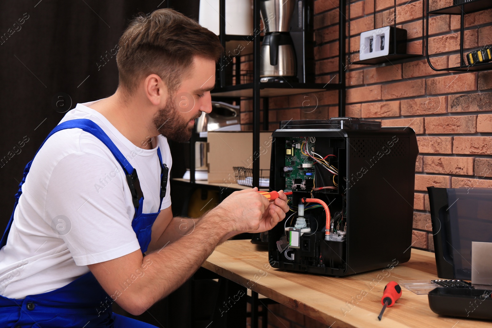 Photo of Repairman with screwdriver fixing coffee machine at table indoors