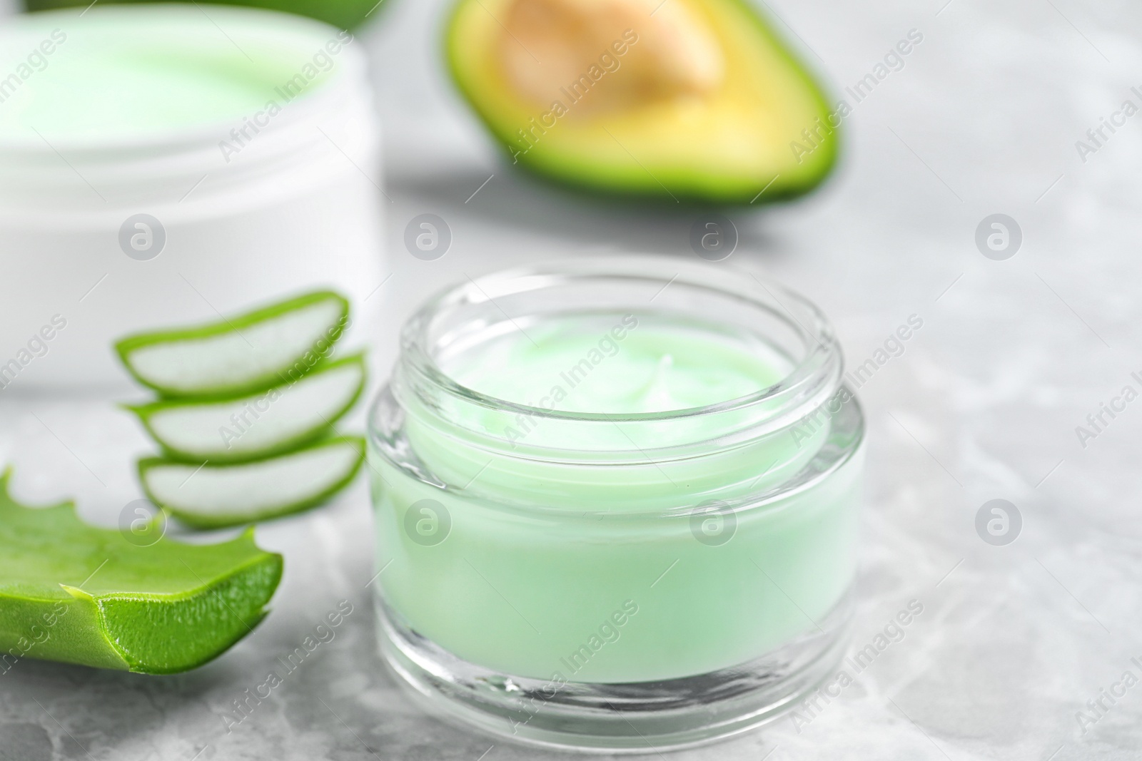 Photo of Open jar of cream and cut aloe on marble background, closeup