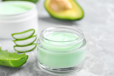 Open jar of cream and cut aloe on marble background, closeup