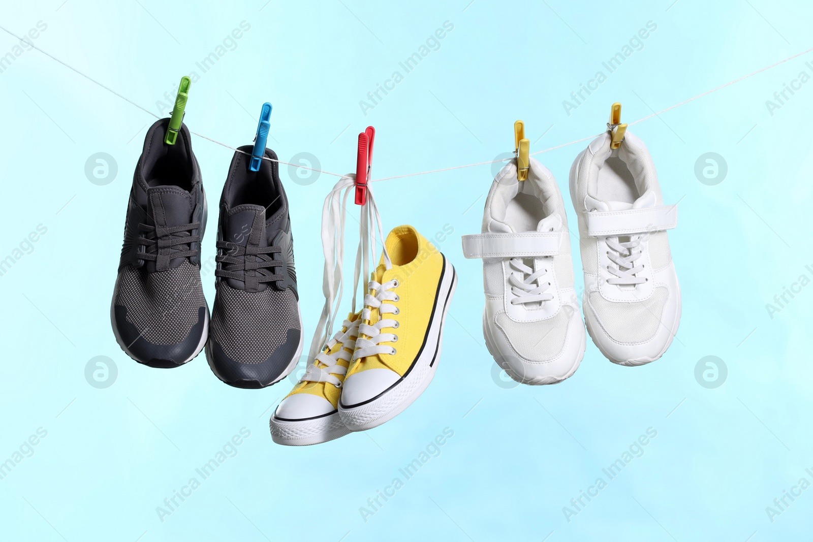 Photo of Different stylish sneakers drying on washing line against light blue background