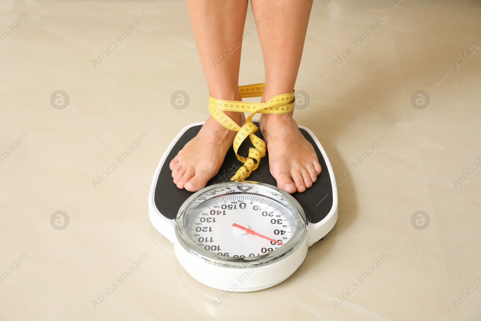Photo of Woman with tape standing on floor scales indoors. Overweight problem