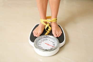 Woman with tape standing on floor scales indoors. Overweight problem