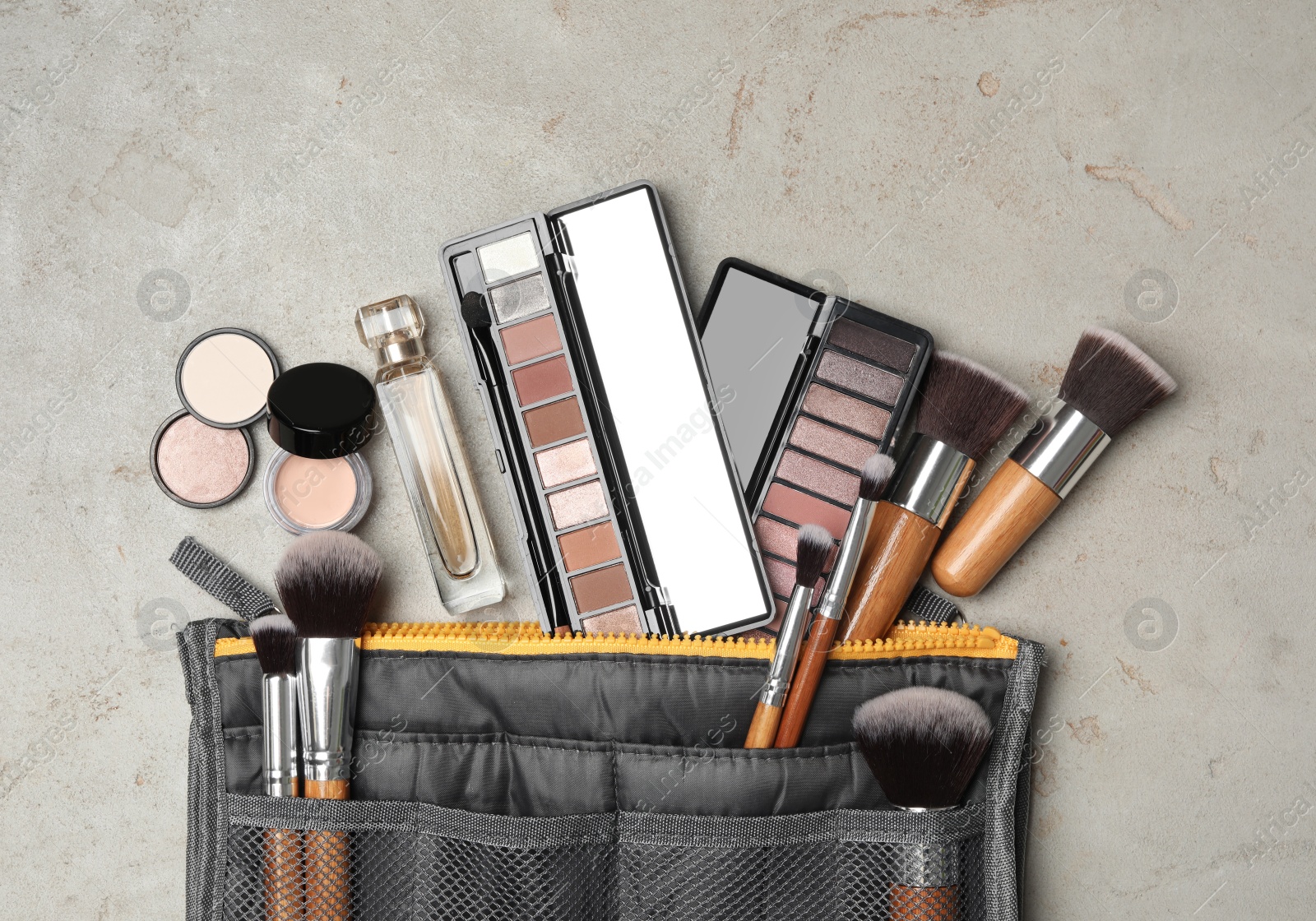 Photo of Cosmetic bag with makeup products on light grey stone background, flat lay
