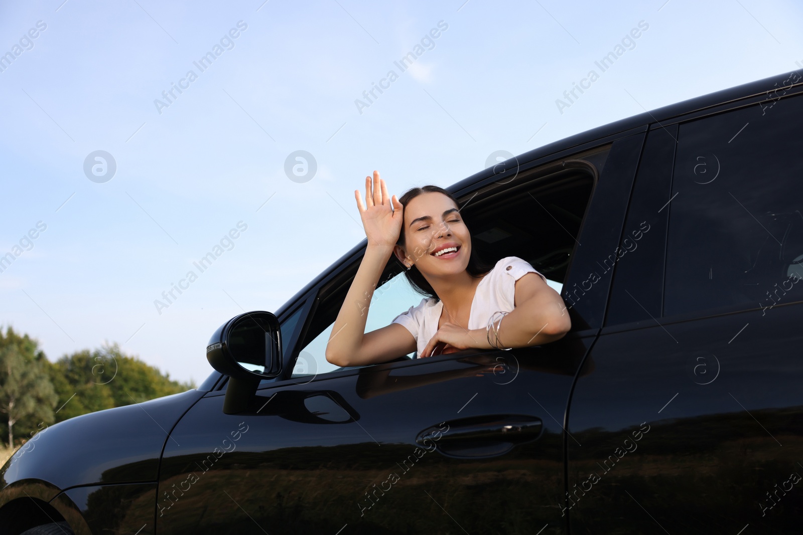 Photo of Enjoying trip. Happy woman leaning out of car window outdoors, low angle view