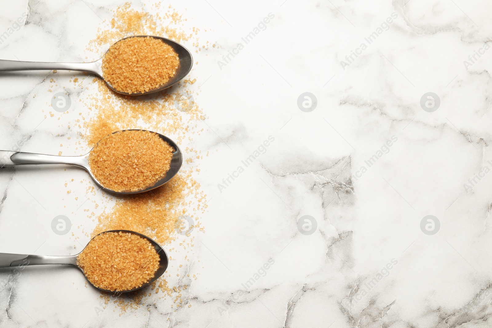 Photo of Spoons with brown sugar on white marble table, flat lay. Space for text