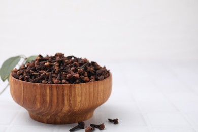 Aromatic cloves in bowl on white tiled table, space for text