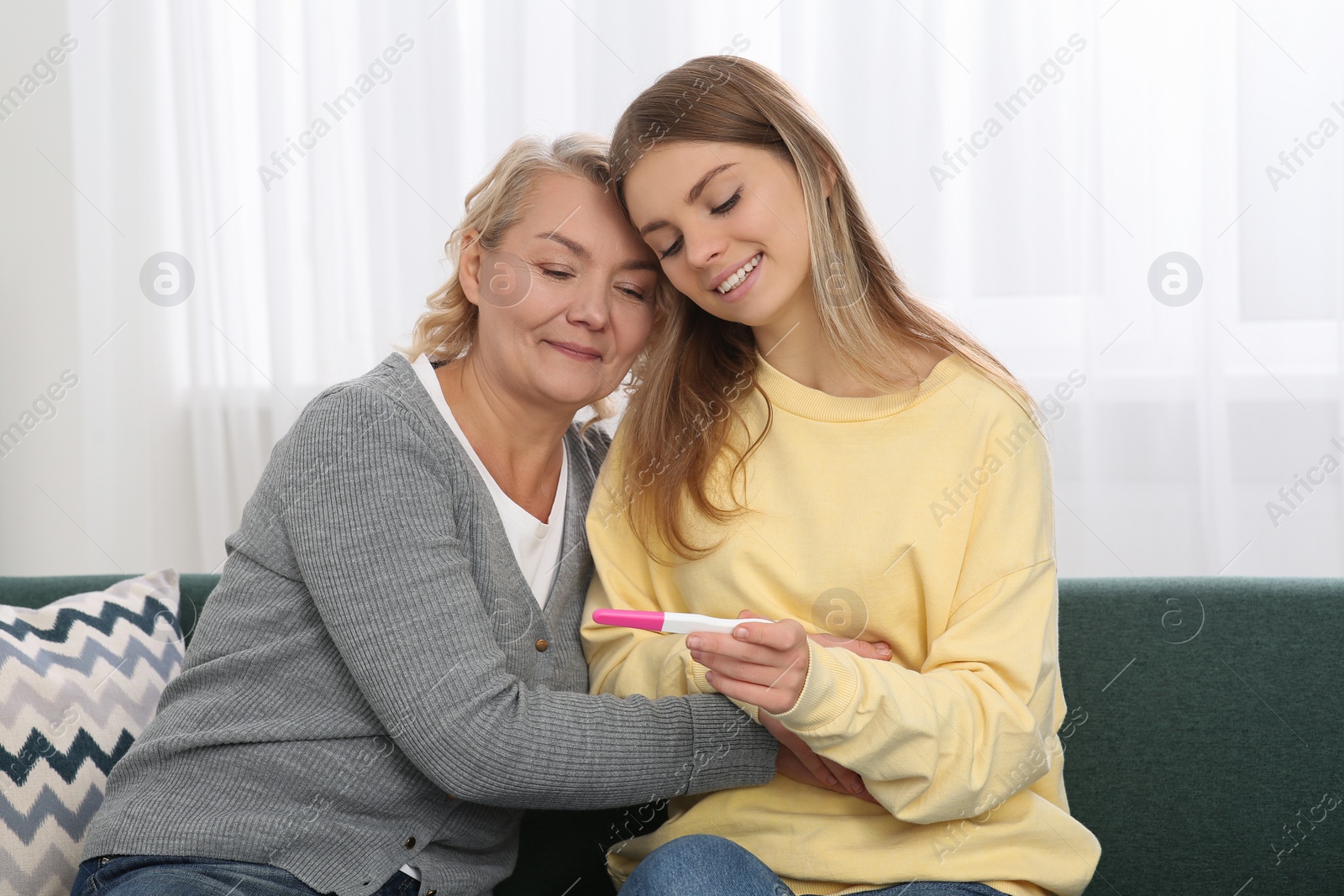 Photo of Young woman showing her mother pregnancy test at home. Grandparent reaction to future grandson